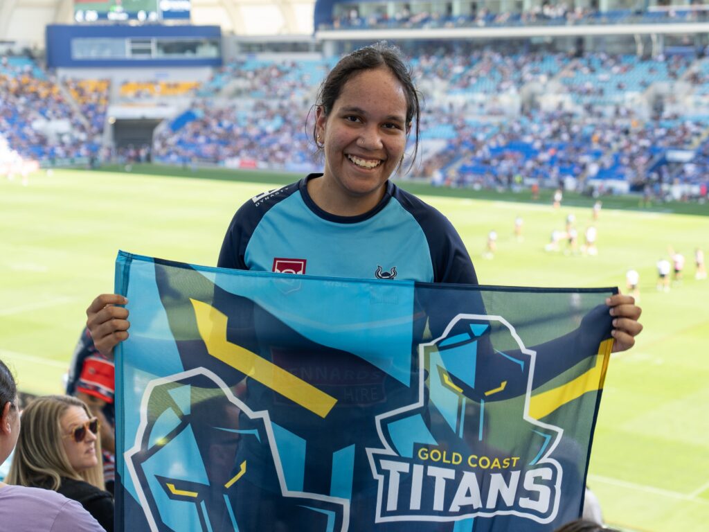 Year 11 Yalari Students holds a Gold Coast Titans flag at CBUS Stadium for the Titans v Roosters game