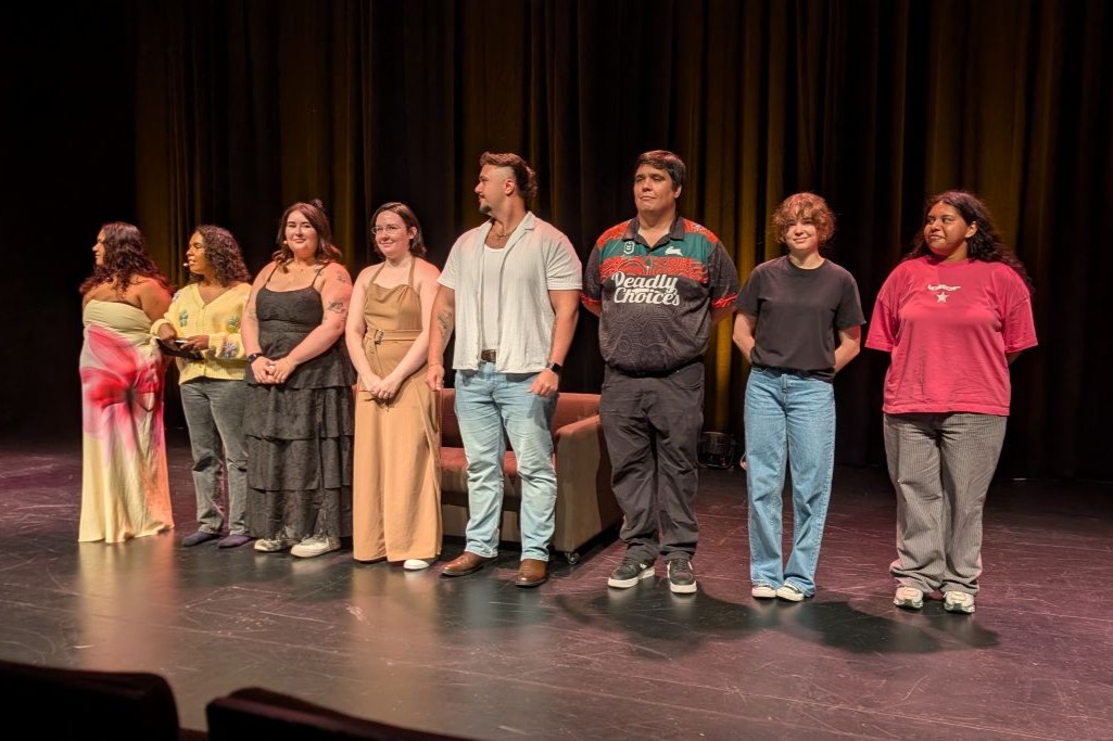 Will munro storytelling 2026 1 - Yalari Eight diverse people stand in a line on a theater stage after a performance facing the audience with a couch behind them yalari