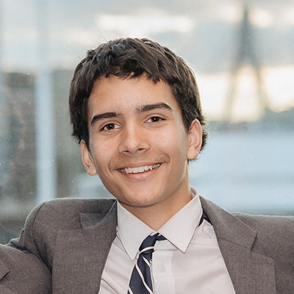 Smiling young man in a gray suit and striped tie indoors with a soft window backdrop   yalari   yalari